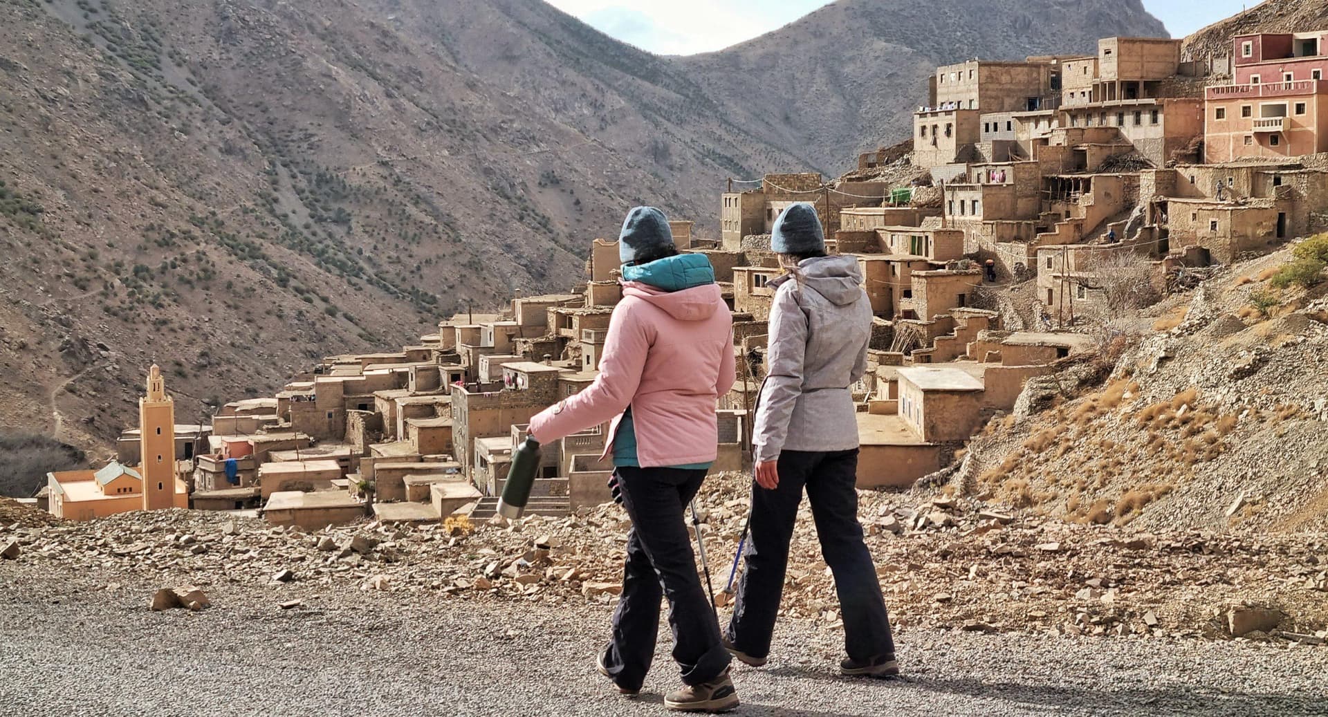 Travelers walking with trekking poles toward a traditional Amazigh village in the High Atlas Mountains